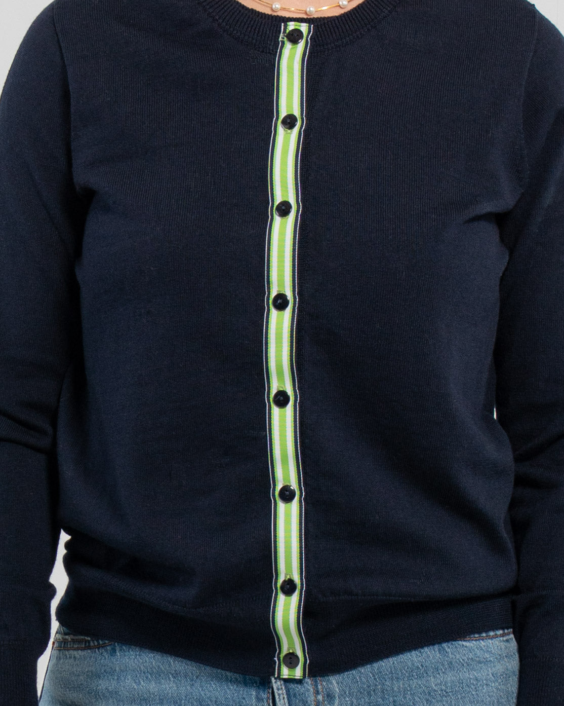 Close up of buttoned navy cardigan with navy pearlized buttons and navy, green and white striped grosgrain ribbon trim.