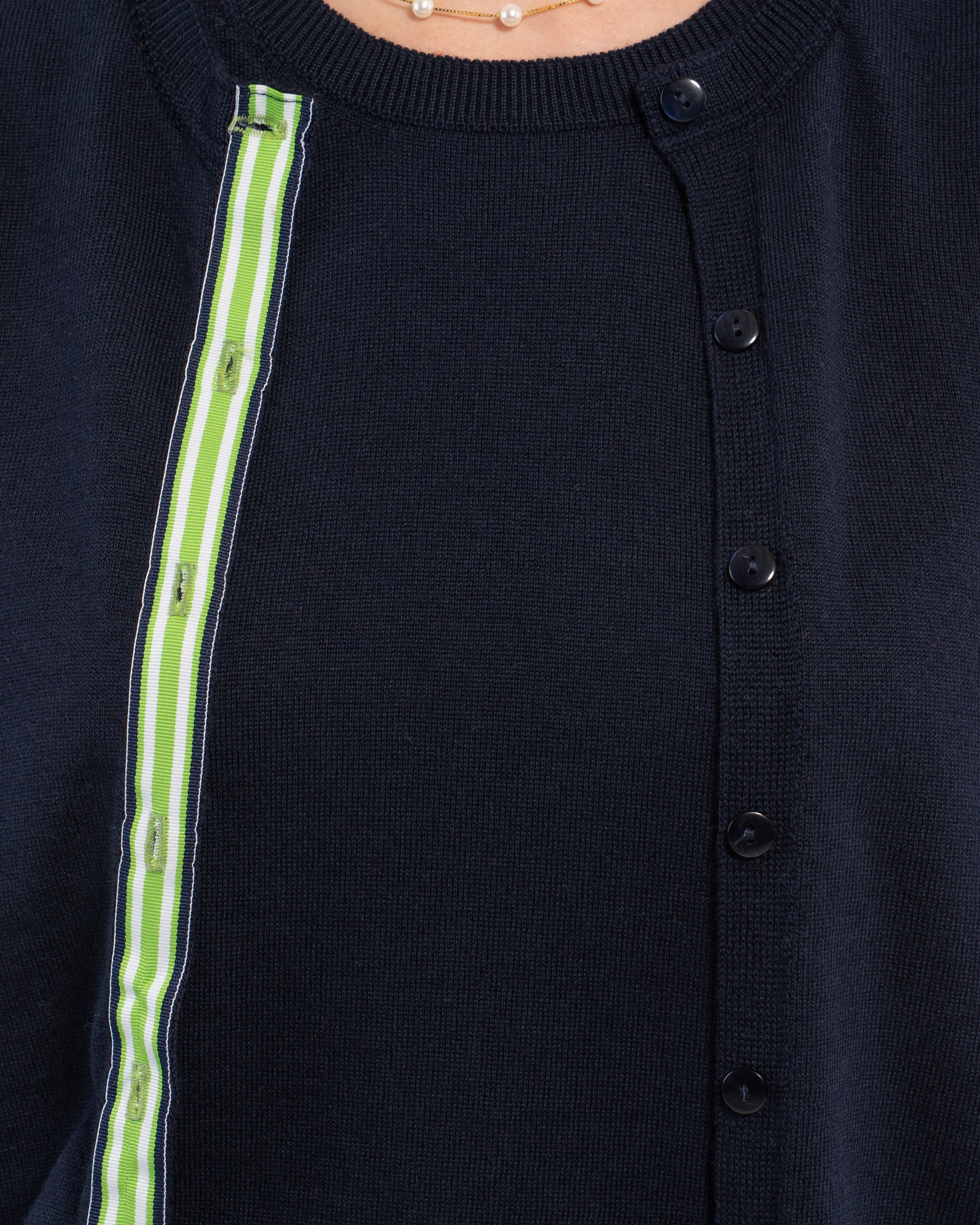 Close up of navy cardigan with navy pearlized buttons and green, white and navy striped grosgrain ribbon over matching navy shell sweater.