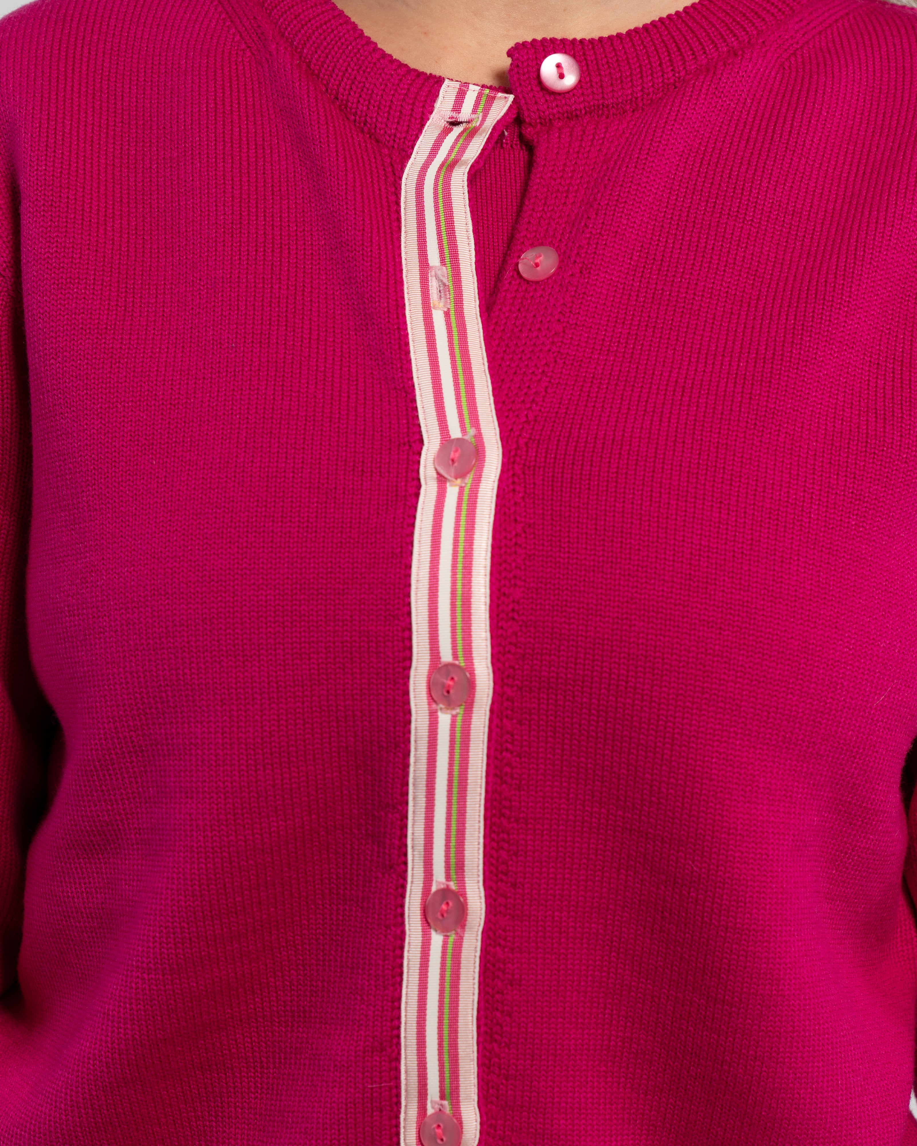 Close up of raspberry pink cardigan with pink pearlized buttons and light pink, dark pink, white, and lime green striped grosgrain ribbon trim.