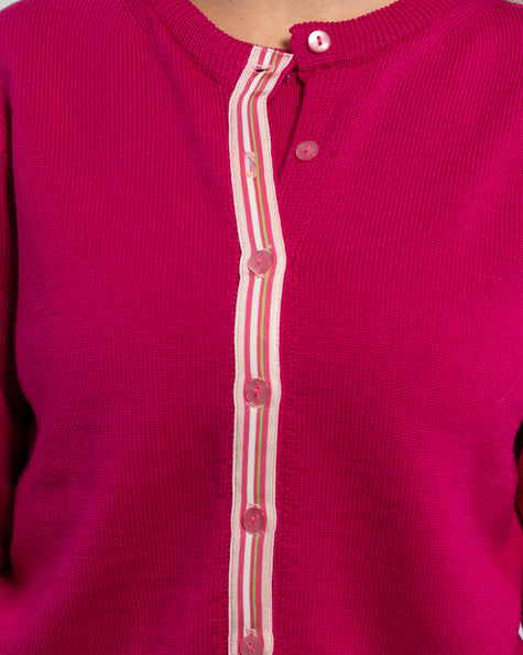 Close up of raspberry pink cardigan with pink pearlized buttons and light pink, dark pink, white, and lime green striped grosgrain ribbon trim.