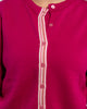 Close up of raspberry pink cardigan with pink pearlized buttons and light pink, dark pink, white, and lime green striped grosgrain ribbon trim.