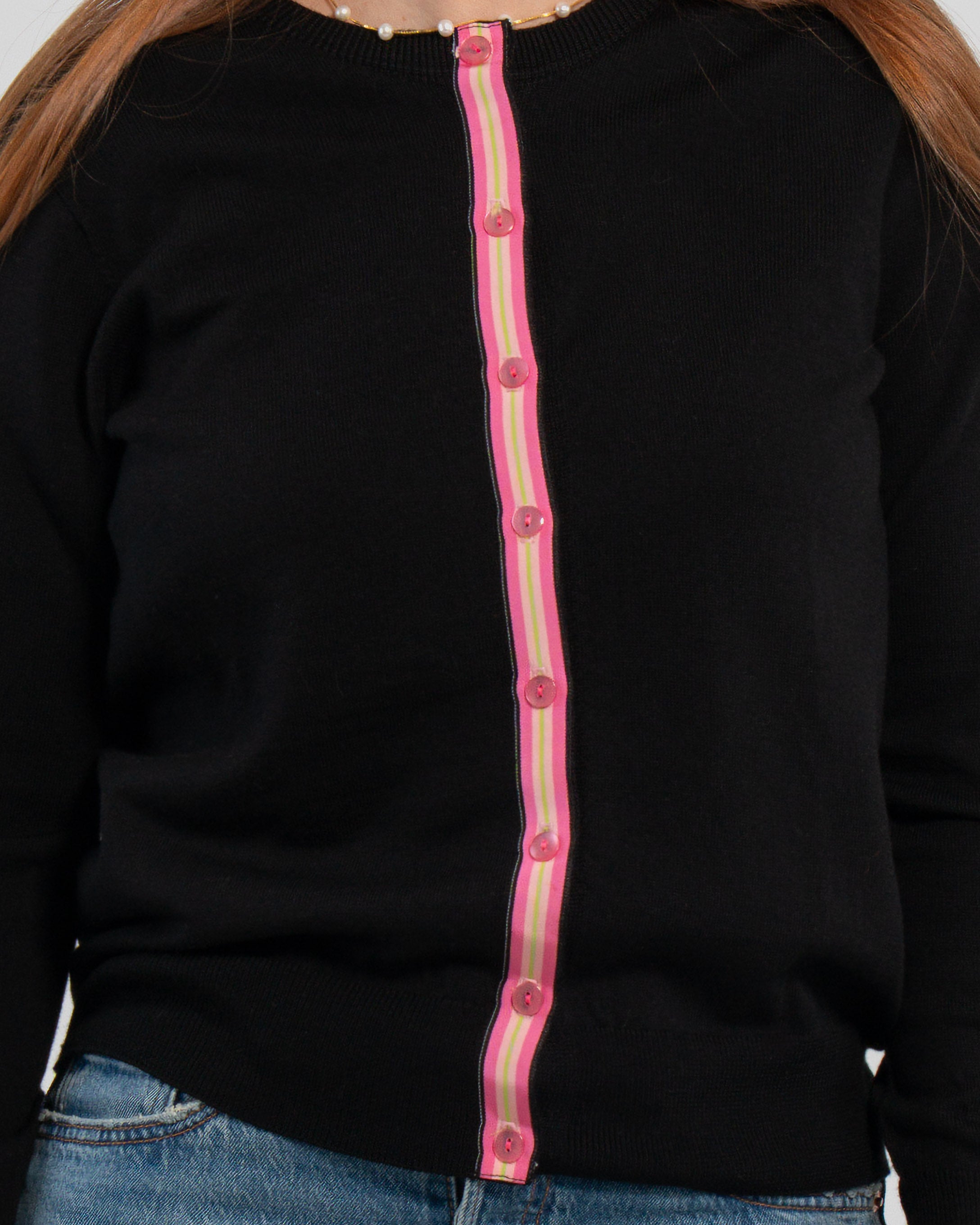 Close up of woman wearing buttoned black cardigan with pink pearlized buttons and hot pink, light pink, and lime green striped grosgrain ribbon trim and jeans.