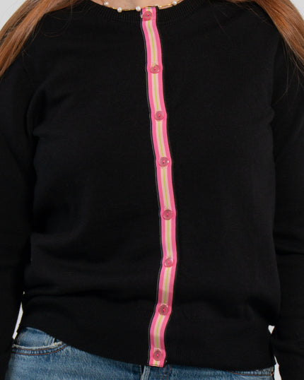 Close up of woman wearing buttoned black cardigan with pink pearlized buttons and hot pink, light pink, and lime green striped grosgrain ribbon trim and jeans.