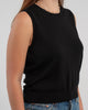 Close up of woman wearing black sleeveless sweater, jeans, pearl choker neckless on plain background.