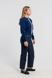 Sideview of woman wearing cobalt blue crop cardigan with pink buttons and rainbow striped grosgrain ribbon trim, jeans, loafers on plain background.