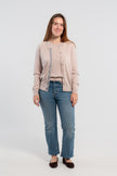 Woman wearing unbuttoned beige cardigan with iridescent shell buttons and tan, purple, lavender, and teal striped grosgrain ribbon over matching beige sweater shell, jeans, ballet flats on plain background,