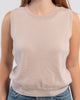 Close up of woman wearing beige sleeveless sweater, jeans, pearl choker neckless on plain background.