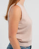 Sideview of woman wearing beige sleeveless sweater, jeans, pearl choker neckless on plain background.