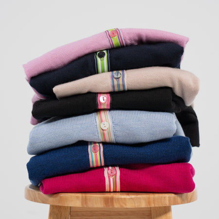 Stack of colorful cardigans on wood stool and plain background
