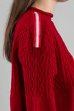 Red cable knit sweater with red, pink and white stripped ribbon trim on shoulder  on a gray background