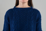 Close up of cobalt blue sweater with cable details and ribbon on shoulders on plain background.