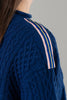 Close-up of shoulder of cobalt blue sweater with ribbon trim with pink, cobalt blue and yellow stripes on plain background.