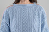 Close-up of a baby blue cable knit sweater with a gray background