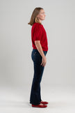 Side view of woman wearing red puff-sleeve cardigan, jeans, red shoes on plain background.
