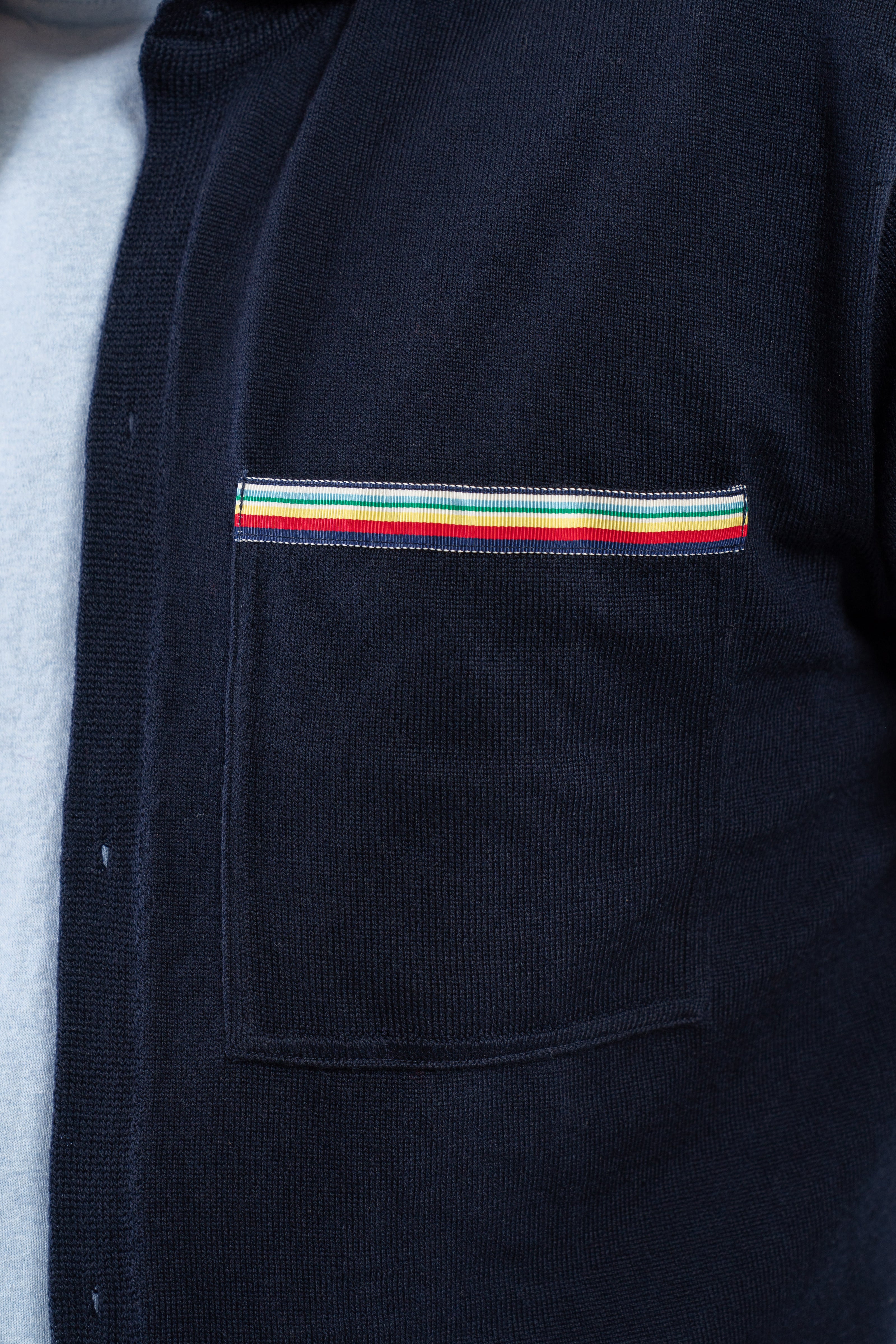 Close up of navy overshirt pocket with ribbon trim with stripes in navy, red, yellow, white, and green.