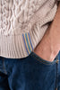 Close-up of person wearing beige cable-knit sweater with purple, tan, and teal striped ribbon trim on hem.