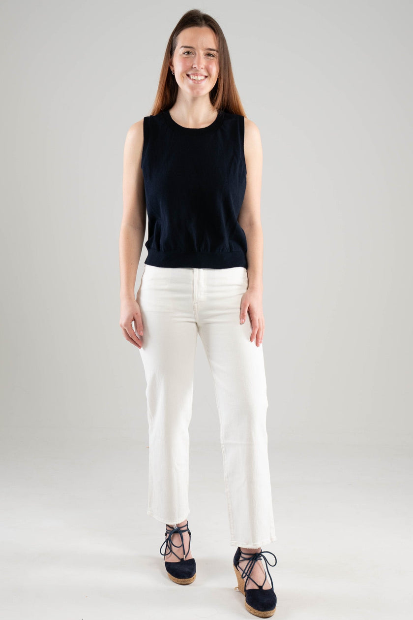 Woman wearing a Noyac Knits navy crew neck sleeveless top in lightweight cotton styled with white pants and navy espadrilles on a white background
