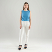 Woman wearing a light blue sleeveless top and white pants on a plain background