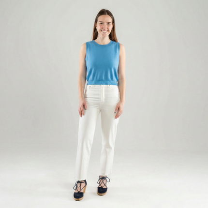 Woman wearing a light blue sleeveless top and white pants on a plain background