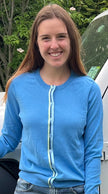 Woman wearing Noyac Knits Allison classic cardigan in sky blue premium cotton and trimmed with green and blue striped ribbon in natural setting outdoors