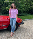 Woman in a Noyac Knits puff sleeve ribbon cardigan in premium lightweight merino styled with barrel jeans and wedges standing next to a red car on a gravel driveway.