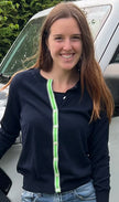 Woman wearing Noyac Knits navy Julie ribbon cardigan trimmed with with green, navy and white striped ribbon over a navy crew neck sleeveless sweater, both in premium Egyptian cotton, styled with  jeans standing in front of white jeep outside