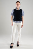 Woman wearing a Noyac Knits classic navy crew neck sleeveless shell styled over a blue and white puff-sleeve, ruffle neck blouse  with white pants and navy espadrilles on a white  background