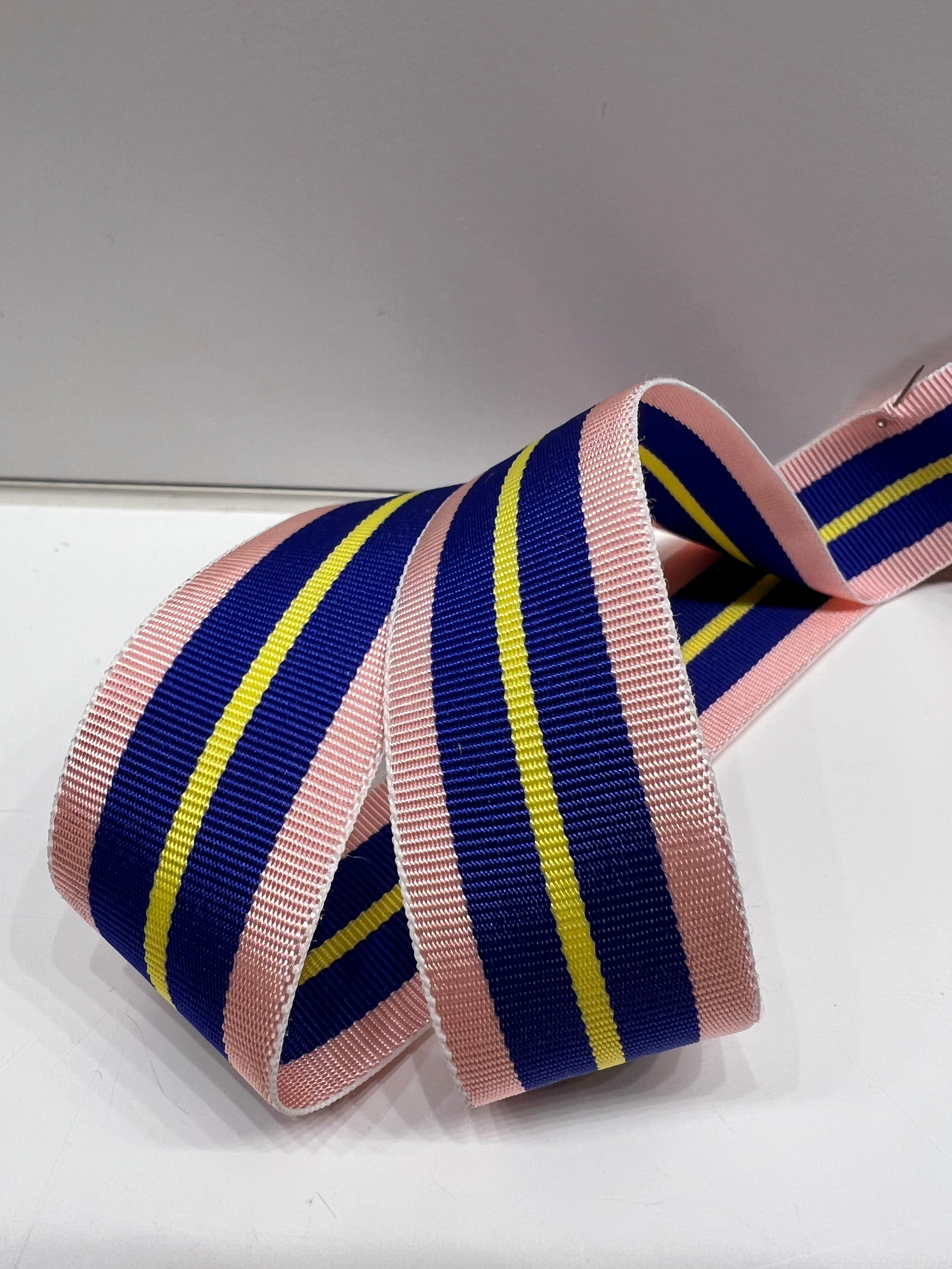 Close up of grosgrain ribbon with pink, cobalt blue and yellow stripes on plain background.