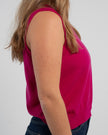 Sideview of woman wearing Noyac Knits raspberry pink sleeveless crop sweater in premium merino wool and jeans on plain background. 