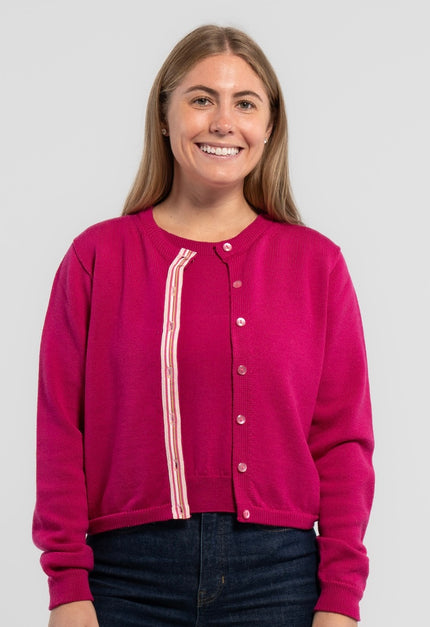 Woman wearing Noyac Knits Grace Cardigan in raspberry pink premium merino wool trimmed with signatrue  pink buttons and pink, white, green striped grosgrain ribbon trim and jeans on plain background.