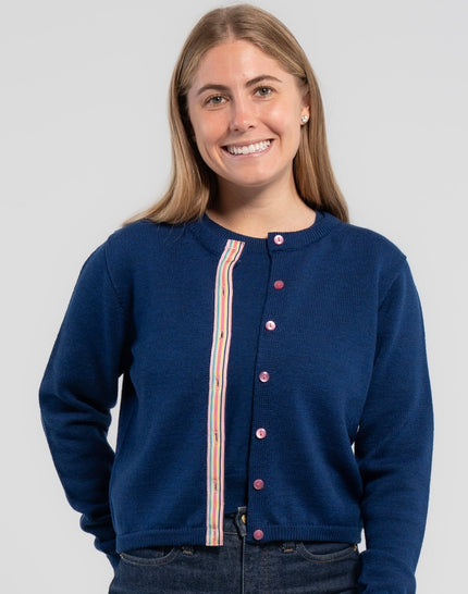 Woman wearing Noyac Knits Sissy Crop Cardigan in gorgeous cobalt blue trimmed with signture pink buttons and rainbow striped grosgrain ribbon -- knit in premium merino - styled with matching merino cobalt blue crew neck sweater shell on plain background.