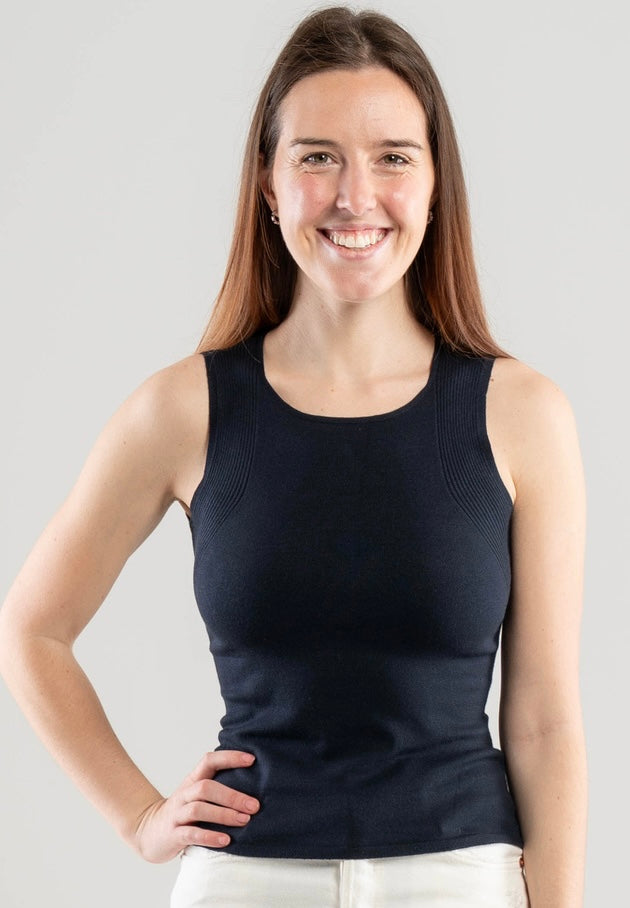Woman wearing a Noyac Knits navy scoop neck tank top in lightweight and soft ecoviscose styled with white pants on a white  background