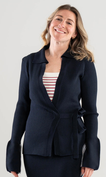 Woman wearing a Noyac Knits navy ribbed wrap sweater over a red and white striped square neck top on a white background