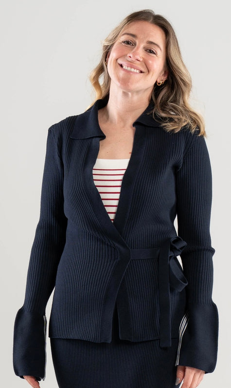 Woman wearing a Noyac Knits navy ribbed wrap sweater over a red and white striped square neck top on a white background