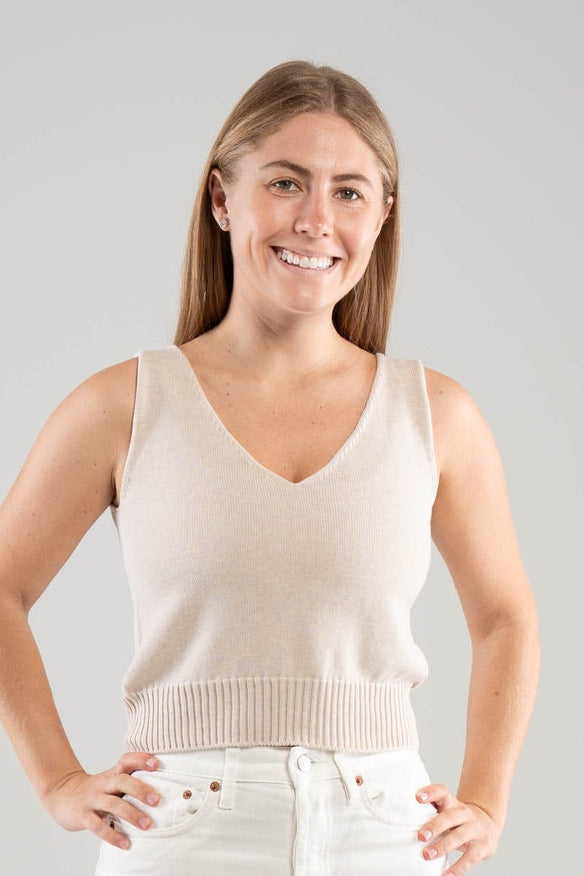 Woman wearing a Noyac Knits light sand colored cotton double v-neck crop tank top styled with white jeans  on a white  background
