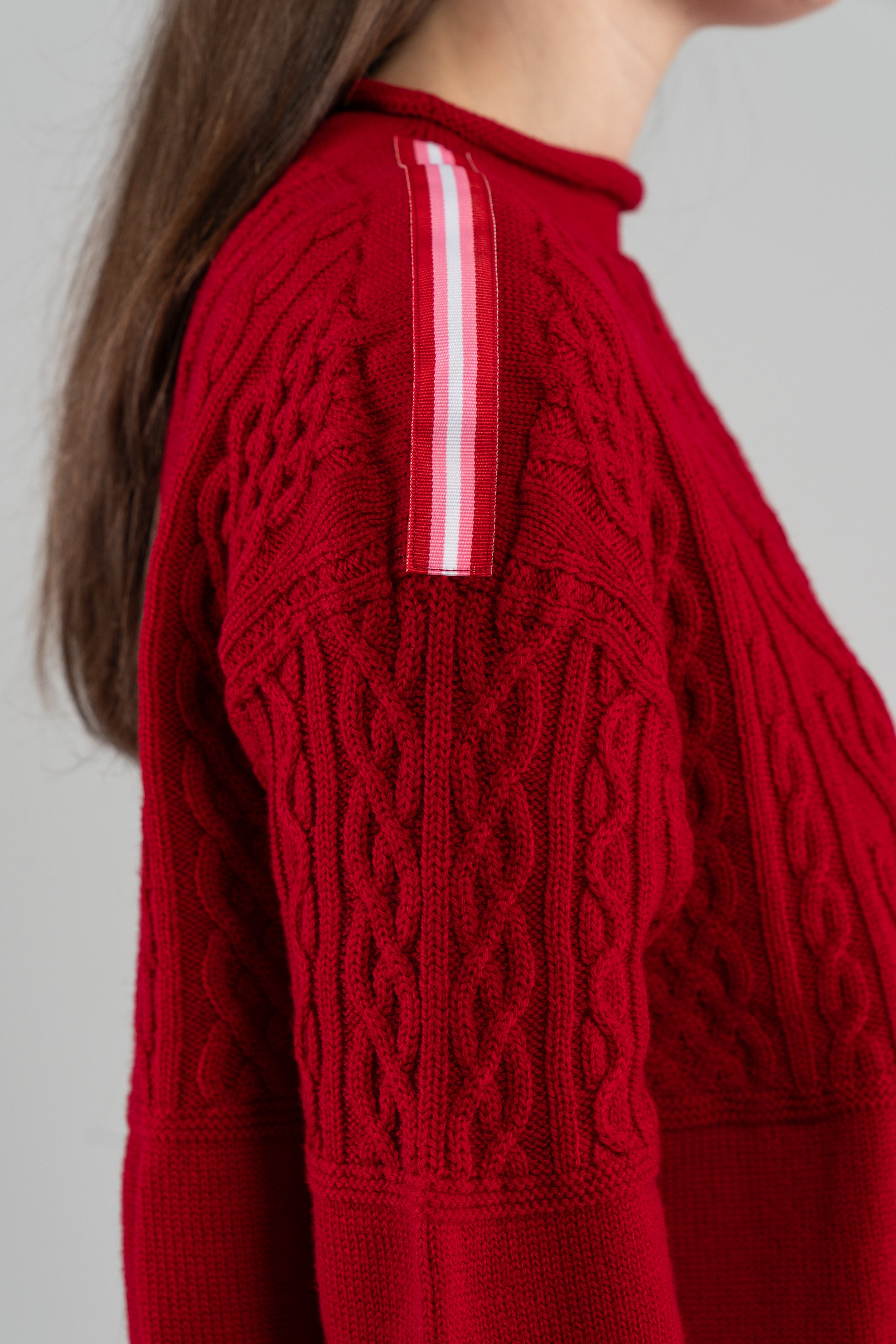 close up of red Noyac Knits boatneck pullover sweater showing beautiful cable knit  pattern and signature ribbon shoulder trim in red, pink and white stripe - knit in premium, soft merino wool