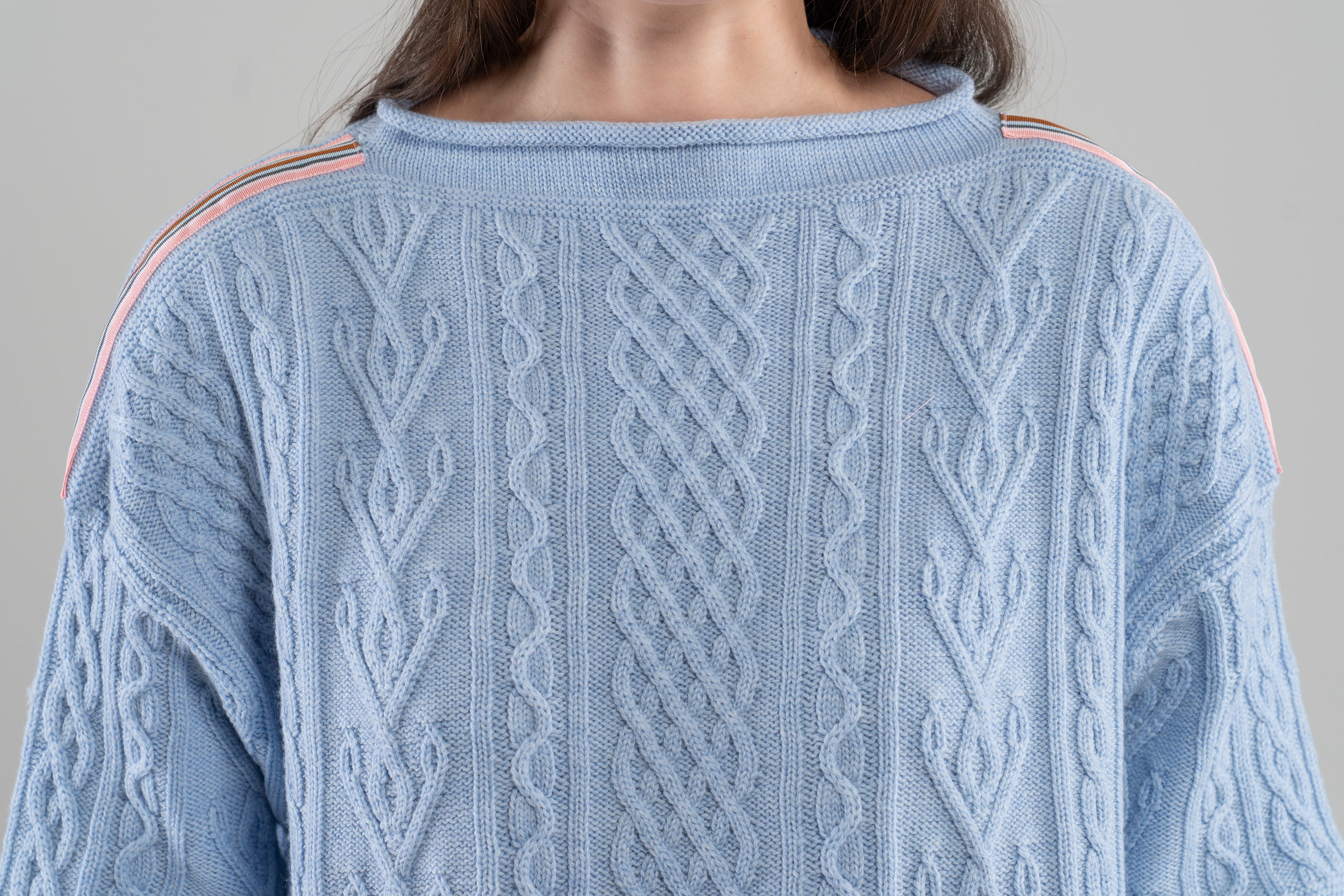 Close-up Noyac Knits Channing boatneck pullover in beautiful baby blue featuring cabling and signature ribbon trim on shoulder, knit in premium soft merino wool  on plain background.