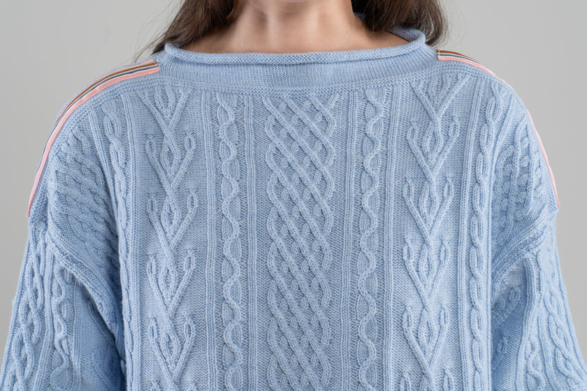 Close-up Noyac Knits Channing boatneck pullover in beautiful baby blue featuring cabling and signature ribbon trim on shoulder, knit in premium soft merino wool  on plain background.