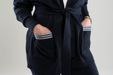 Close up of navy and white striped ribbon-trimmed pockets on navy blue Noyac Knits  long belted cardigan made in cozy soft ecoviscose against white background