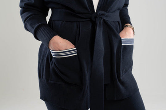 Close up of navy and white striped ribbon-trimmed pockets on navy blue Noyac Knits  long belted cardigan made in cozy soft ecoviscose against white background