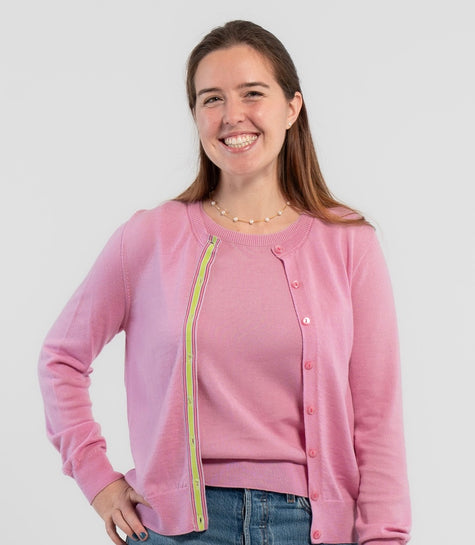 Picture of woman wearing Noyac Knits orchid pink cardigan with pink buttons and  signature ribbon trim in stripes of green, pink and lilac -- knit in ultrasoft premium merino wool, styled with pearl choker necklace and jeans on plain bakckground.