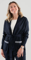 Woman wearing a Noyac Knits navy blue long belted cardigan with navy and white striped ribbon-trimmed pockets made in cozy soft ecoviscose on a plain background