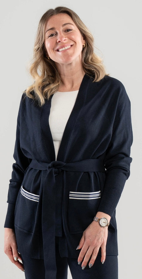 Woman wearing a Noyac Knits navy blue long belted cardigan with navy and white striped ribbon-trimmed pockets made in cozy soft ecoviscose on a plain background